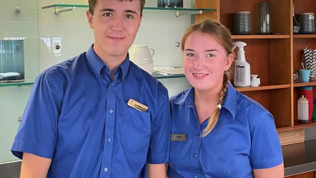 Friendly hotel staff in blue uniforms ready to welcome guests, standing in a modern reception area with stylish decor.