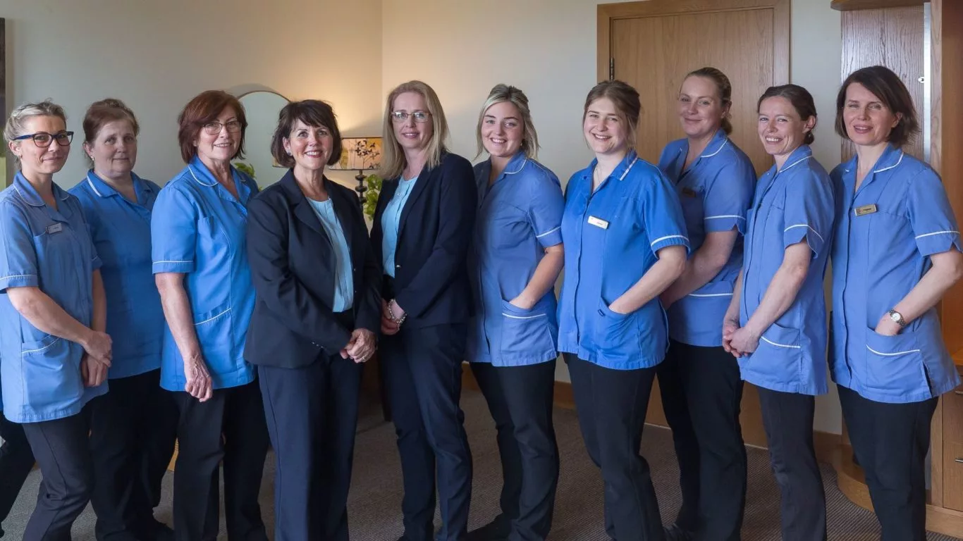Friendly hotel staff in blue uniforms standing together, ready to offer an exceptional guest experience in a welcoming lobby.