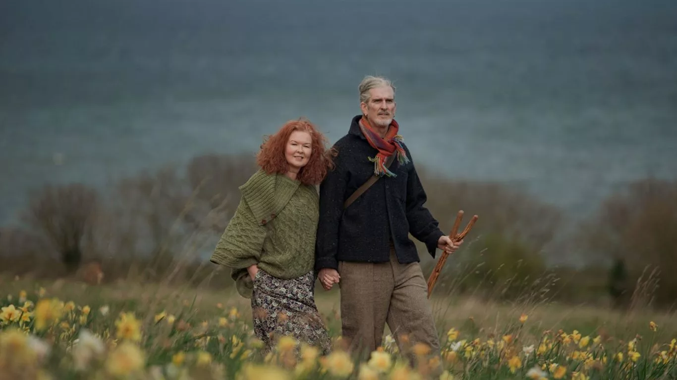Couple enjoys a peaceful walk through a daffodil field with ocean views, offering a tranquil countryside escape.