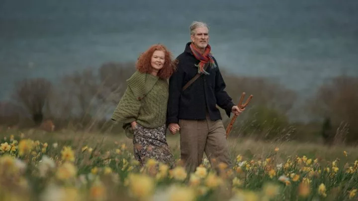 Couple enjoys a peaceful walk through a daffodil field with ocean views, offering a tranquil countryside escape.