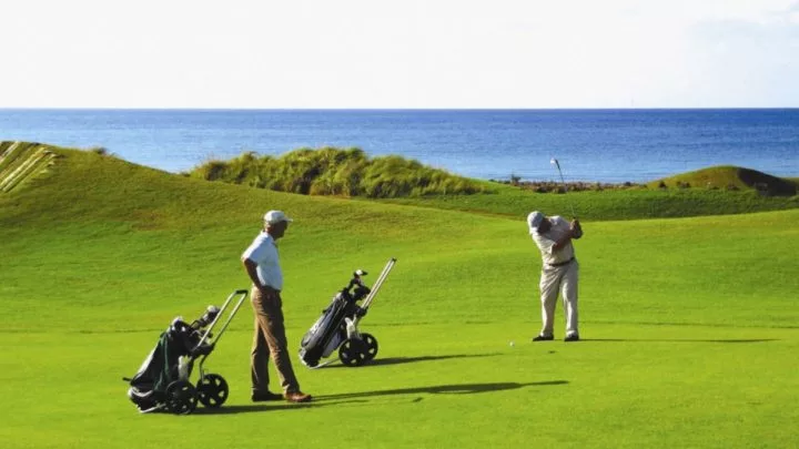 Guests enjoy a round of golf on a lush course with ocean views, clear skies, and rolling greens, perfect for relaxing getaways.