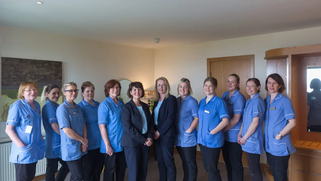 Friendly hotel staff in blue uniforms welcome guests warmly in a cosy, well-lit lobby.