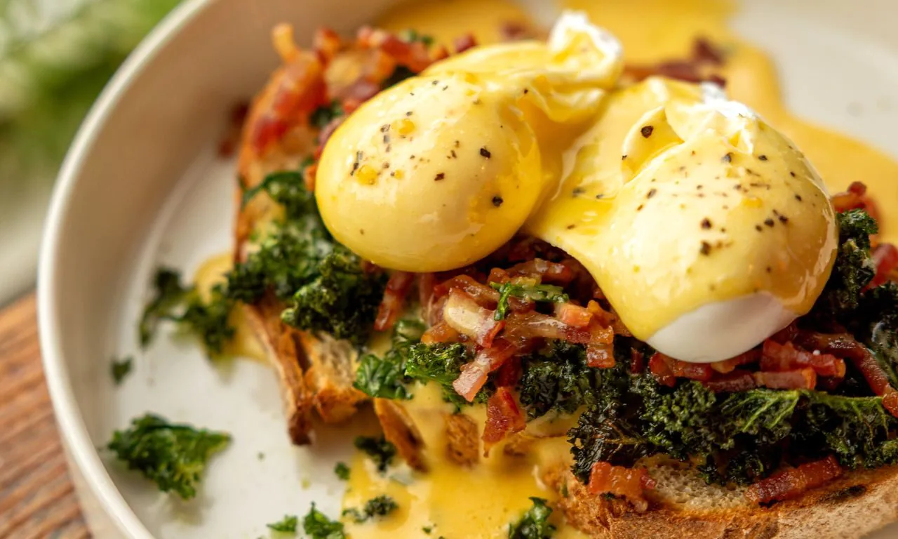 Delicious eggs Benedict on artisan toast with fresh greens and bacon, highlighting gourmet breakfast at our luxurious hotel.