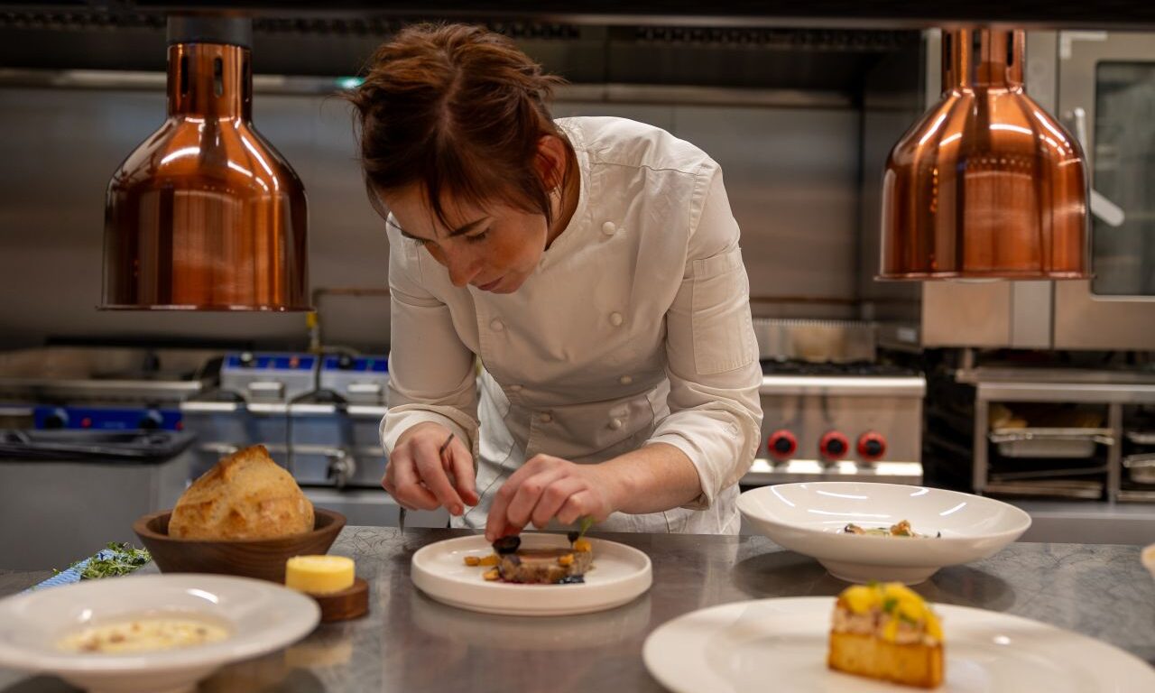 Chef carefully plates gourmet dish in hotel&rsquo;s elegant kitchen, reflecting luxury dining experiences and culinary excellence.