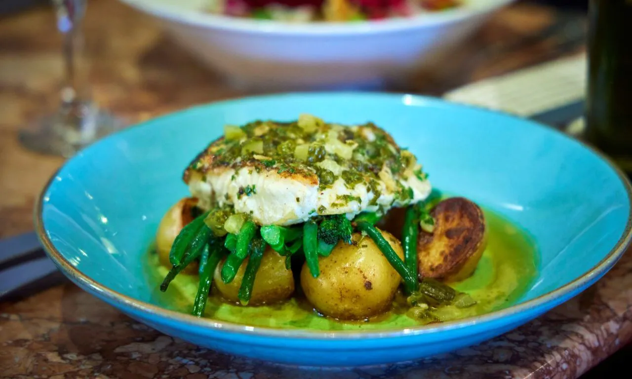 Delicious herb-crusted fish with green beans and potatoes on a blue plate, perfect for a relaxing hotel dining experience.